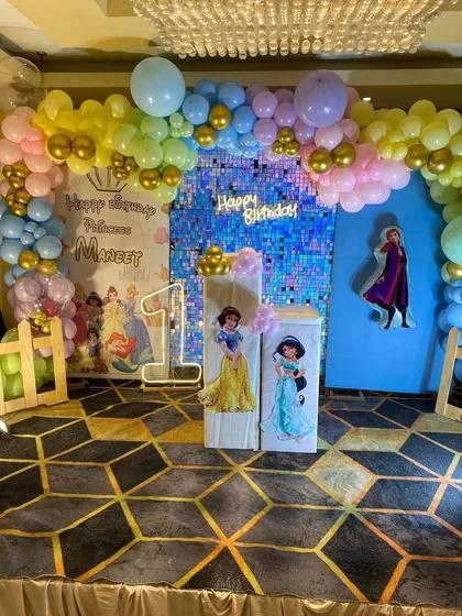 A wide shot of the complete Disney Princess first birthday setup. The combination of the pastel balloon arch, shimmer wall, character cutouts, and marquee number creates a magical photo corner.