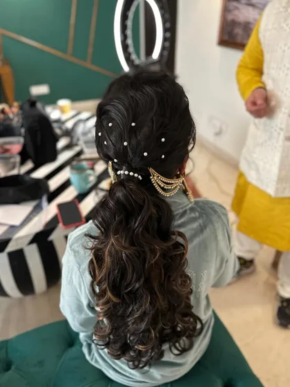 A messy ponytail for a Mehndi look, adorned with scattered pearls and a traditional passa-style accessory at the base.