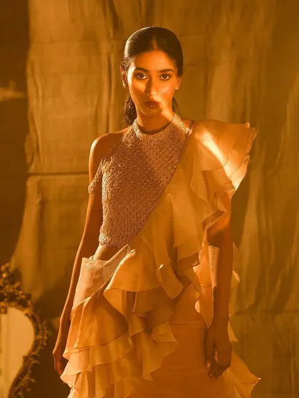 A stunning portrait featuring a model in a ruffled organza saree. The makeup is warm and glowing, with bronzed skin and a soft smokey eye that complements the golden hour lighting, creating a truly ethereal bridal look.