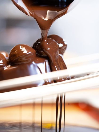 The perfect chocolate drip. A close-up of rich, tempered dark chocolate being poured over a dessert, a satisfying moment in any chocolate making process.