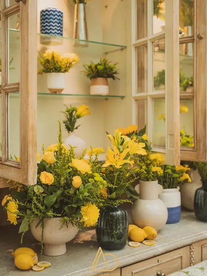 A close-up of the floral arrangements inside the cabinet, showcasing the variety of yellow blooms and the fresh lemons scattered throughout.