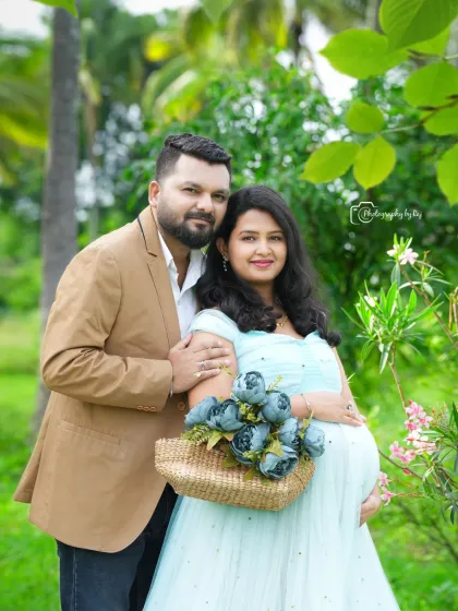 A lovely couple's portrait in a garden, with the mother-to-be holding a basket of blue flowers in a matching light blue gown.