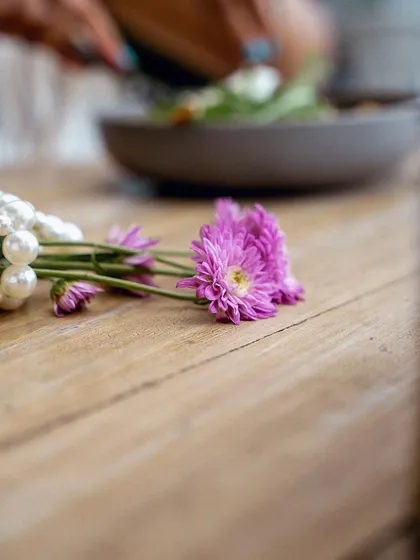 An atmospheric detail shot from the Olive Bistro series. The focus on flowers and a pearl necklace on the wooden table helps build a romantic and elegant mood.