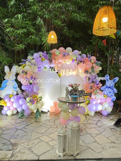 A wide view of the 'Oh Babies' outdoor setup at night, with beautiful lighting enhancing the pastel balloon arch and bunny theme.