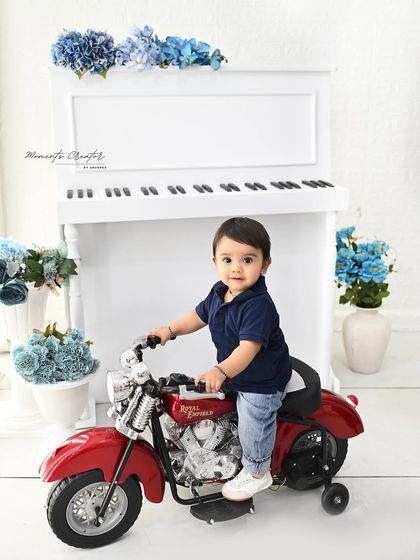 This little man is ready to ride. The classic red toy motorcycle and the clean, bright studio setup with a white piano create a cool and stylish portrait for a first birthday.