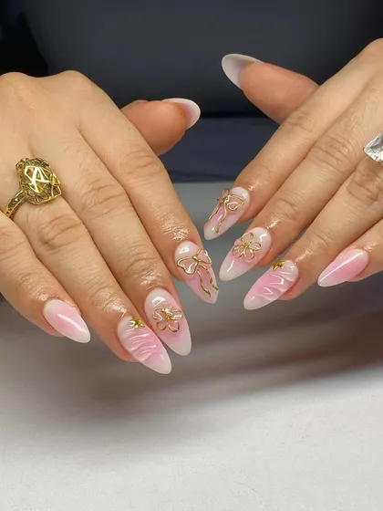 A soft and romantic design. These pink ombre nails are decorated with delicate 3D gold bow charms and textured accents.