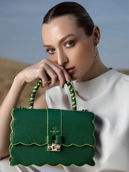 A close-up beauty and accessory shot for Da Milano. The styling is clean and minimal, with a simple white top and sleek hair, allowing the unique, scalloped-edge green handbag to be the hero of the image.