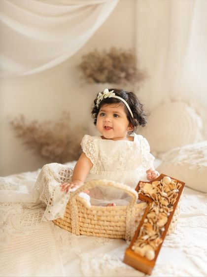 This one-year-old is sitting in a wicker basket, part of a neutral, bohemian-inspired studio setup for her first birthday portraits.