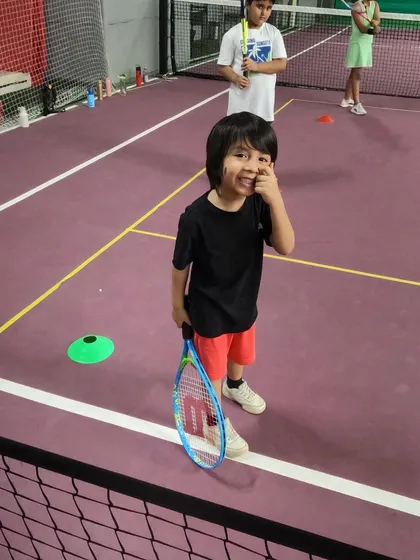 A happy player from our Red Batch, racket in hand and ready to learn. We focus on positive reinforcement to build a lifelong love for the game.