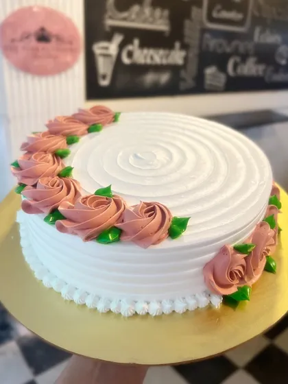 A simple white cake with a spiral top and a crescent of delicate dusty rose buttercream flowers.
