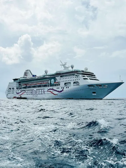 A dramatic shot of the Cordelia cruise ship on the open sea. The perspective emphasizes the vessel's size and the vastness of the ocean, creating a sense of adventure and escape.