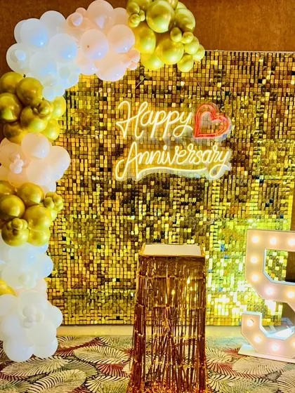 Celebrating a golden 50th anniversary in style. This glamorous photo corner includes a shimmering gold sequin backdrop, large light-up marquee numbers, and an elegant organic balloon arch in white and gold.