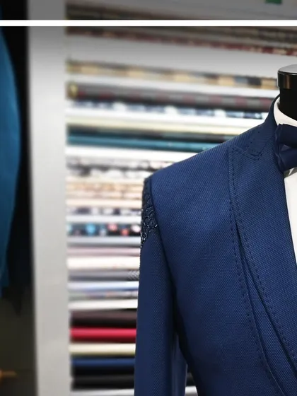 A close-up shot of a blue tuxedo jacket, highlighting the texture of the fabric and the detailed stitching.