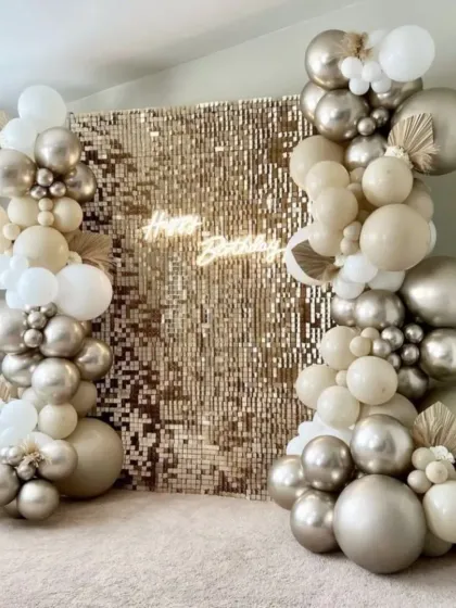 A sophisticated party setup with a champagne gold sequin wall. The balloon arrangement in shades of beige, white, and silver chrome creates a neutral yet glamorous look.