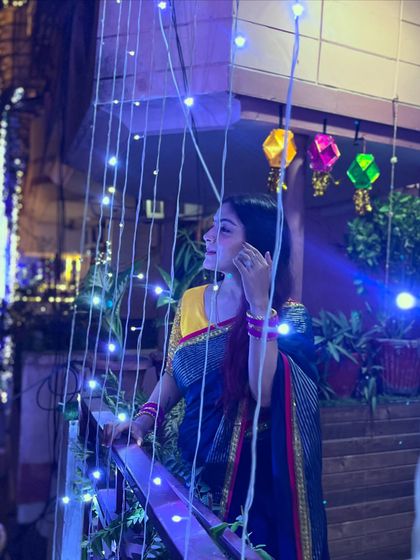 Enjoying the Diwali lights from the balcony. The combination of a bright yellow blouse with a dark blue saree creates a beautiful contrast for evening celebrations.