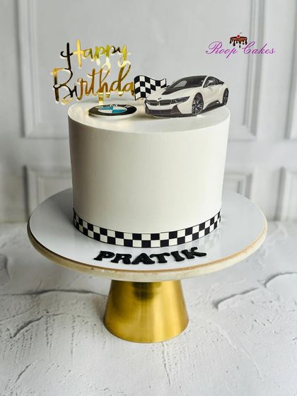 A sleek BMW-themed cake for a car enthusiast. The design features a checkered racing stripe, the BMW logo, and a car topper, perfect for a high-speed birthday celebration.