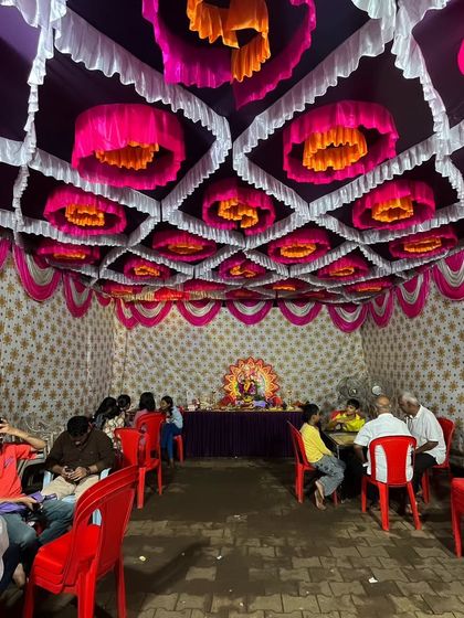A beautiful pandal ceiling decorated with pink, orange, and white drapes for a Ganpati festival celebration. This kind of intricate ceiling work makes the pandal feel grand.