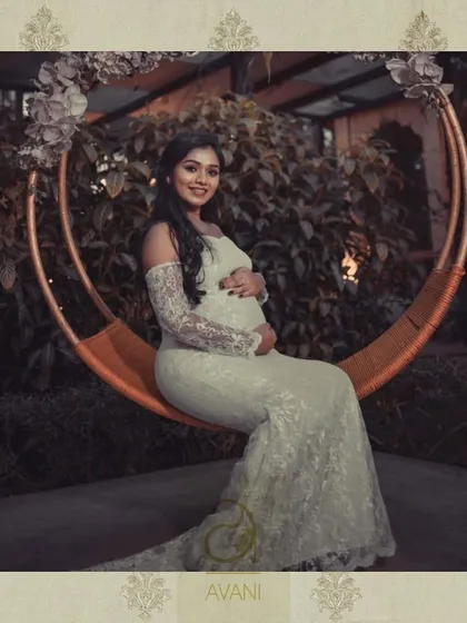 A stunning maternity photoshoot featuring a custom-designed white lace gown. The off-shoulder design and long train create a look of ethereal beauty.