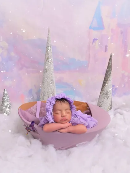 A single newborn twin, dressed in a whimsical purple bonnet, sleeps in a pastel-colored, snowy castle scene. This portrait highlights the individual, fairy-tale-like setups I can create even within a twin session.