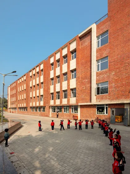 Students line up in the courtyard of HRM Global School, Delhi. The use of exposed brick and human-scaled design creates a warm and inviting atmosphere, making the school feel like a second home.