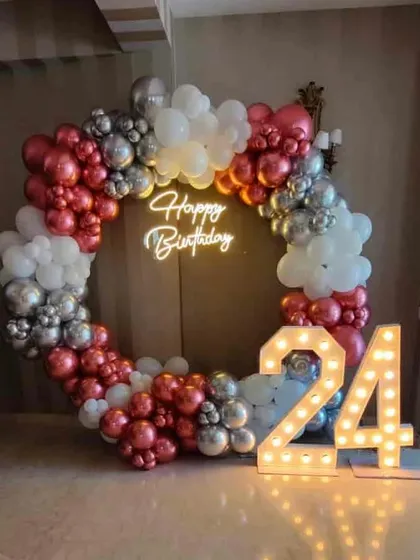 A classy 24th birthday decoration with a red, white, and silver balloon ring. The setup is completed with large marquee numbers.