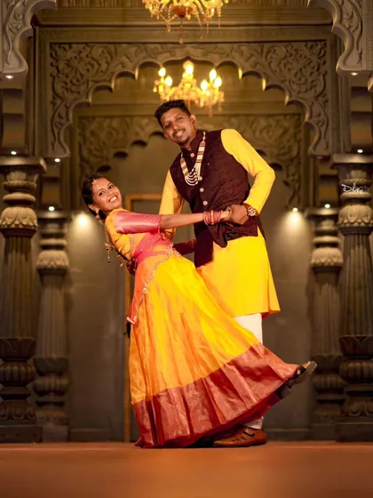 A fun, dance-like pose in a grand hall. This shot captures the joy and celebration of the couple's journey in their beautiful traditional outfits.