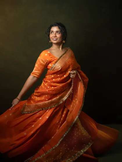 Movement and color come together to tell a story of joy and transformation. Vennela, in a vibrant orange saree, embodies the confidence she has cultivated over her journey from a shy child to a global entrepreneur. This shot captures the pure, uninhibited energy of a woman who has found her voice.