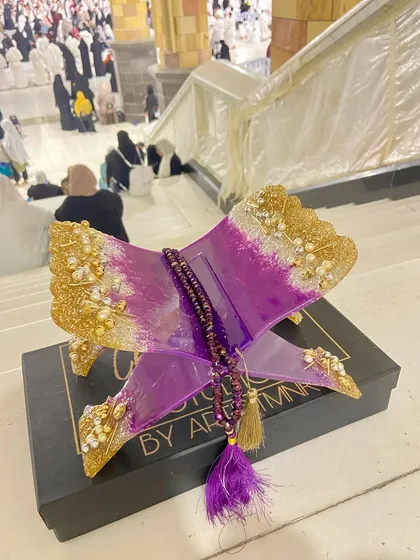 This striking Quran holder is made with a vibrant purple and gold resin design. It comes with a matching crystal tasbeeh and is shown here at the holy city of Makkah, adding to its spiritual significance.