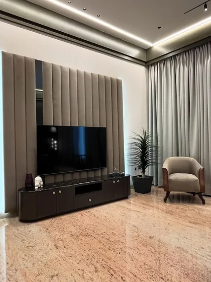 A closer look at the TV unit in the master bedroom. The wall features soft, vertical upholstered panels and a central mirror, creating a sophisticated backdrop. The dark, curved console adds a touch of modern elegance.