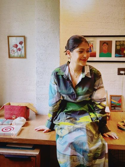 A woman sitting on her desk, surrounded by her art and personal treasures. This environmental portrait is full of color and personality.