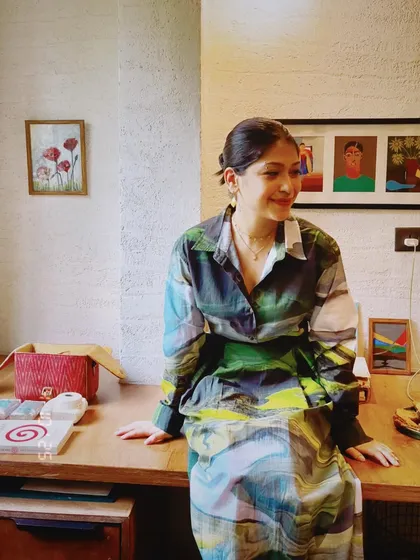 A woman sitting on her desk, surrounded by her art and personal treasures. This environmental portrait is full of color and personality.