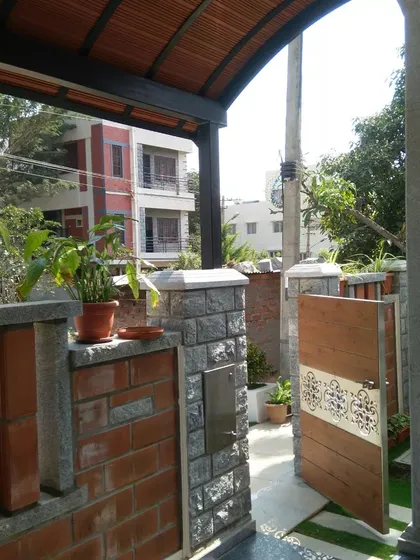 The entrance gate and compound wall, combining stone, brick, and wood for a cohesive and natural aesthetic.