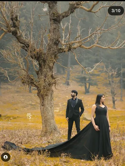 A dramatic and moody portrait set in a stark, beautiful landscape. The contrast of the elegant black gown against the rustic trees creates a powerful and artistic pre-wedding image.