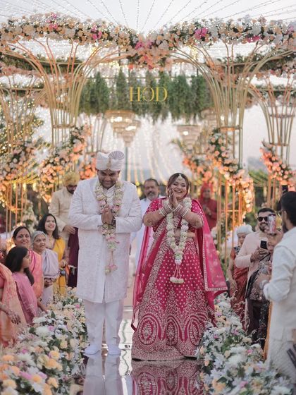 The couple sharing a moment of prayer and gratitude on the mirrored aisle, surrounded by lush flowers and the grand mandap.