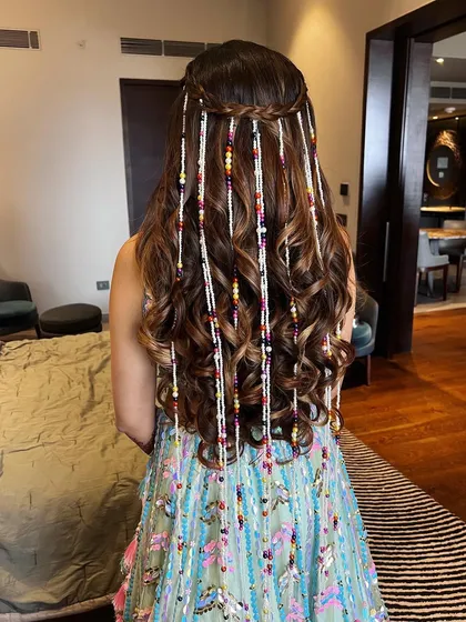 A unique half-up hairstyle featuring soft curls and long, beaded strands that match the outfit. This is a creative and bohemian look, perfect for a carnival or Mehendi event.
