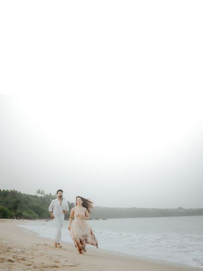 The couple runs joyfully along the beach, with waves crashing beside them. This action shot captures their energy and the wild beauty of the Goan coastline.