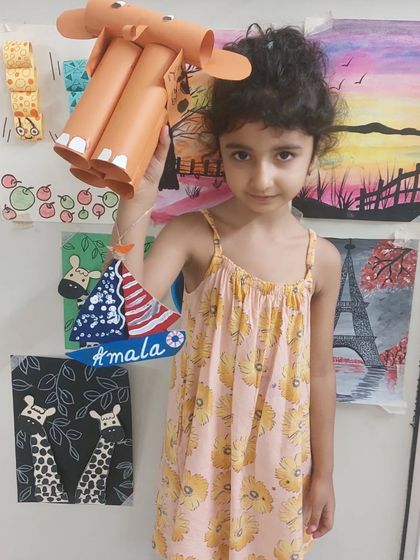 This student is proudly holding up two different crafts she made: an upcycled elephant and a personalized wooden boat nameplate.