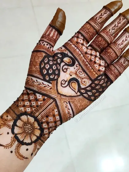 This image shows how a minimal design on the back of the hand can be paired with a fuller pattern on the palm. Here, the floral cuff is combined with a peacock-themed palm design.