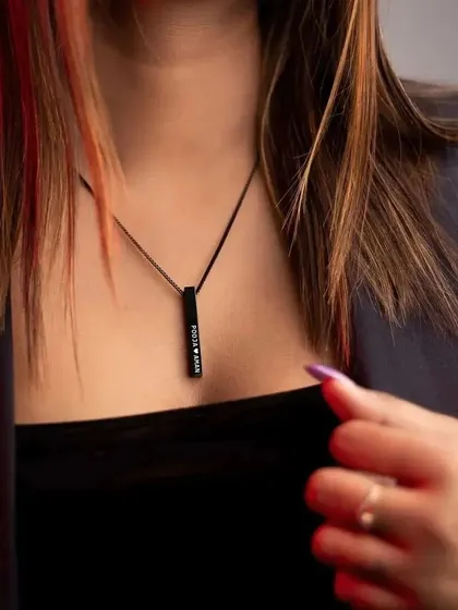 A woman wearing a black bar pendant engraved with two names and a heart. This shows how the bar style can be used to celebrate a relationship.