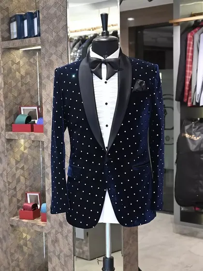 A classic party look. This navy blue velvet tuxedo jacket is adorned with silver polka dots, offering a playful yet elegant style. The black satin lapel provides a sharp, classic contrast.