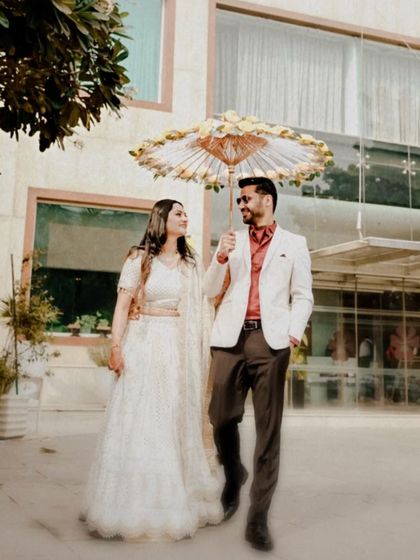 A whimsical and stylish shot of a couple walking under a decorative umbrella, blending traditional elements with a modern, chic aesthetic for their engagement photos.