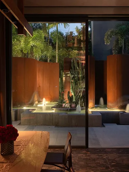 The view from a dining table inside KEUS, looking out onto the illuminated Corten steel and water feature. The landscape provides a stunning, dynamic backdrop for the interior space.