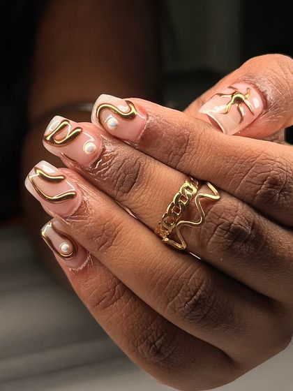 A detailed shot of the sculpted gold swirls and pearl accents. This design plays with negative space and texture, making it a sophisticated choice for those who love unique nail art.