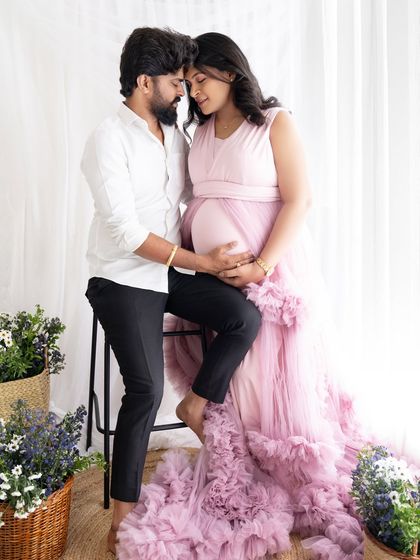 A tender moment captured with the couple looking at each other, their hands on the baby bump, surrounded by soft floral decor.