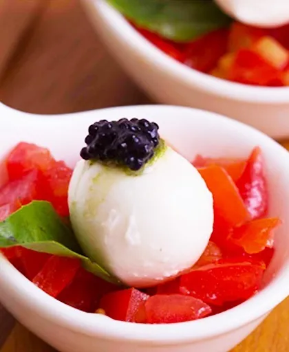 A close-up of a vegetarian caprese bite, featuring a mozzarella ball with a balsamic pearl on a bed of diced tomatoes. This appetizer is a perfect example of how we use molecular gastronomy to elevate classic flavours.