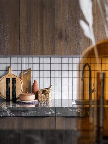 The kitchen features a backsplash of simple white tiles, which provides a clean, graphic contrast to the dark marble countertop and rich wooden cabinets.