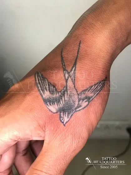 A realistic tattoo of a swallow in flight on the hand, a classic symbol of travel and return.