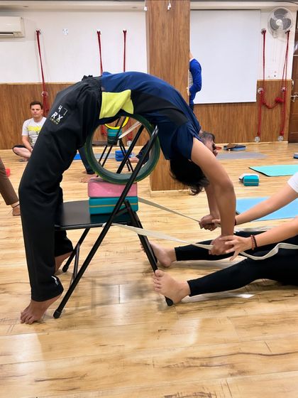 With the help of a partner and props like a chair, wheel, and strap, this student is able to explore a deep backbend with confidence and stability.