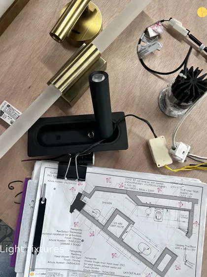 Light fixtures and plans laid out on a workbench at the 58WV site. Selecting the right lighting is a detailed process that involves balancing aesthetics, functionality, and the overall mood of the space.