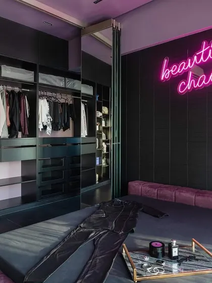 This open-concept wardrobe uses glass doors to create a boutique-like display for clothes and accessories. The dark, moody color scheme paired with the neon sign gives the room a bold, personal feel, proving that a wardrobe can be a central design feature of a bedroom.